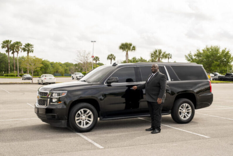 A professional chauffeur for black car service Orlando stands in front of the car to give luxury and comfortable transportation.