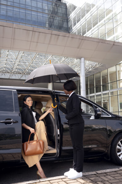 A professional lady chauffeur opens the door of the corporate limousine for the client with style to make the client special